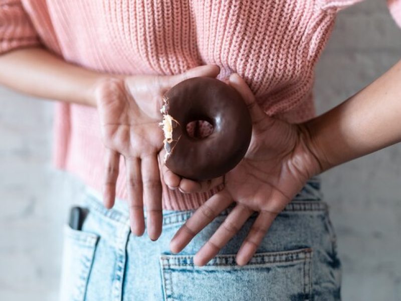 close-up-de-jovem-segurando-uma-rosquinha-de-chocolate-nas-costas-conceito-de-alimentos-pouco-saudaveis_519356-1712